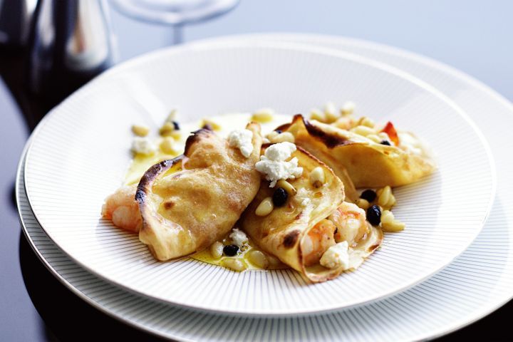 Crespelle With King Prawns, Burnt Butter, Currants And Pine Nuts in a white bowl.