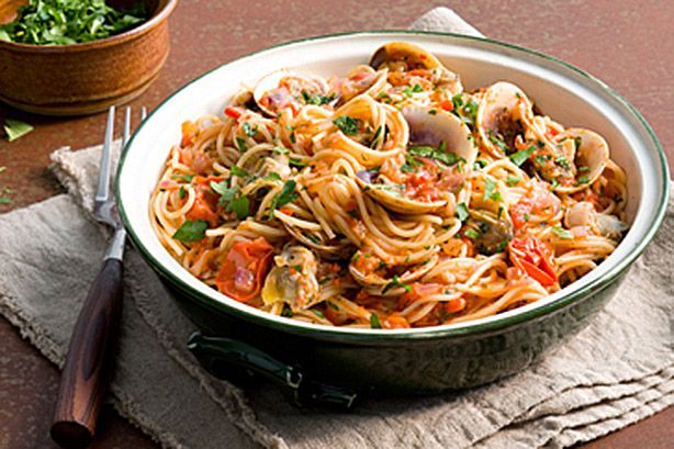 Spaghettini With Clams And Cherry Tomato presented in black dish.
