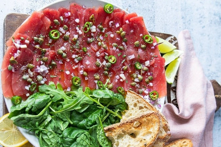 Tuna Carpaccio dislayed on white plate.