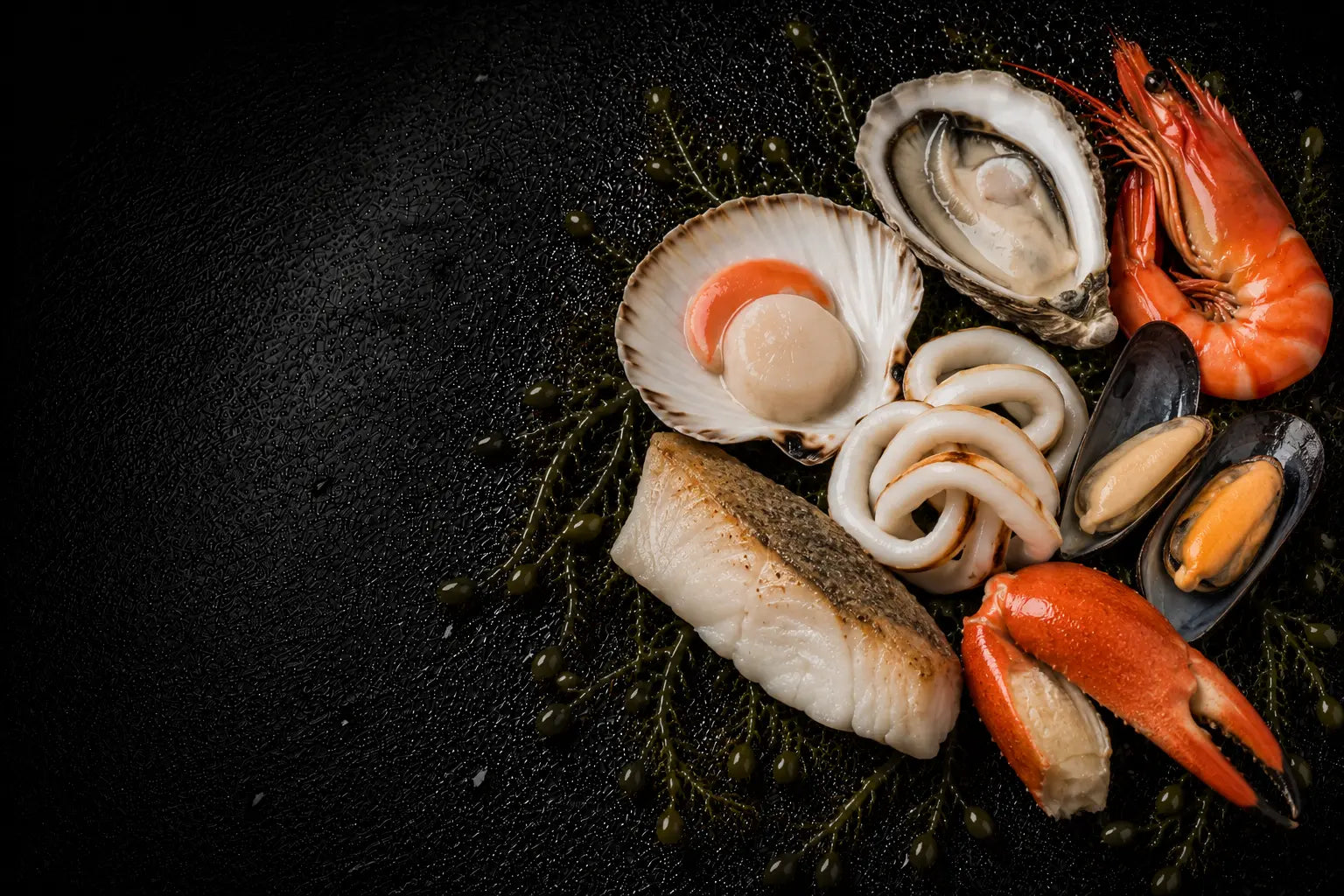 Assorted seafood including oysters, shrimp, and crab legs on a dark surface.