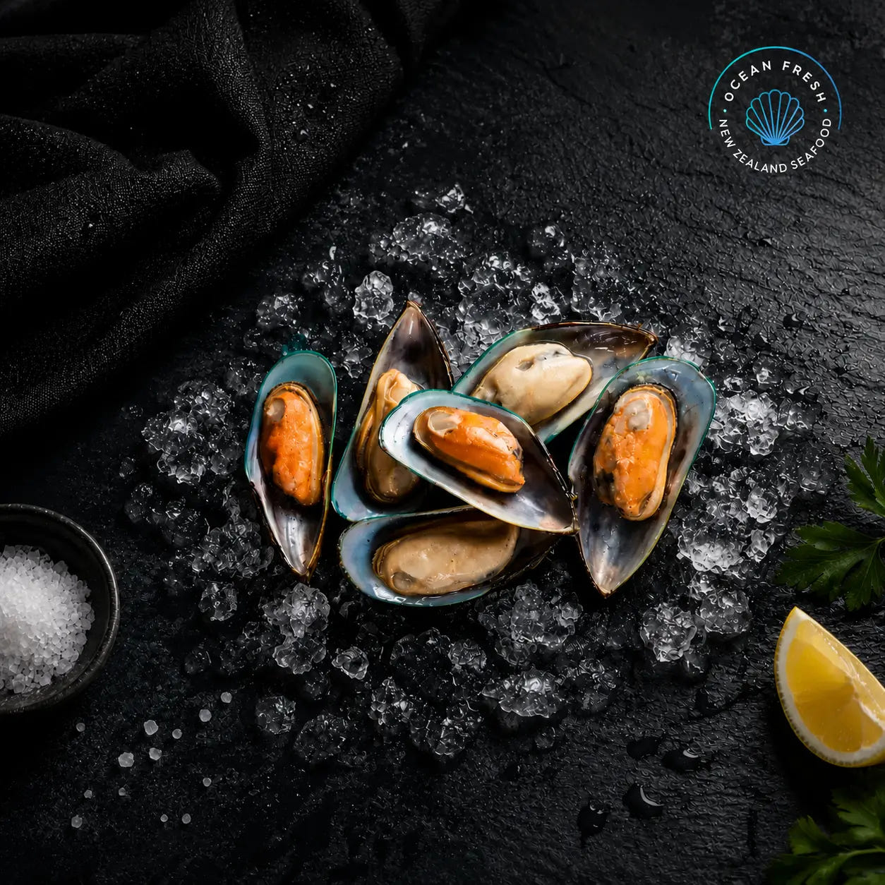 Frozen New Zealand greenlip mussels in half shells displayed on black slate with lemon
