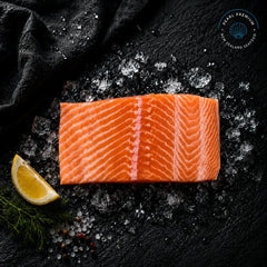 Fresh ora king salmon portions arranged on black slate over crushed ice with lemon
