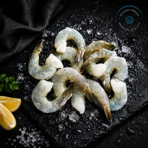 Frozen peeled prawn cutlets with tails arranged on black slate with crushed ice and lemon
