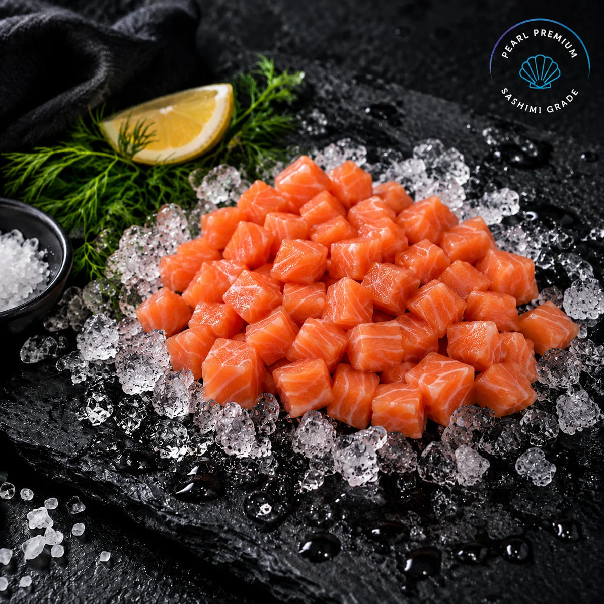 Finely diced raw salmon sashimi cubes arranged on crushed ice on a dark slate platter, with a lemon wedge, dill, and a small bowl of salt nearby. A 'Pearl Premium Sashimi Grade' logo is visible in the top right corner.