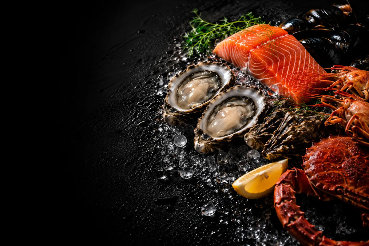 A seafood platter on a black surface with ice, featuring two open oysters, orange salmon slices, dark mussels, a red lobster claw, a lemon wedge, and green herbs.