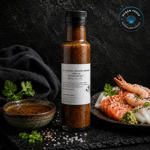 Bottle of Soy & Ginger Japanese Dressing presented on dark stone beside prepared seafood